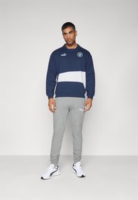 Hanorac bleumarin cu dungi albe orizontale, având guler polo și logo. Combinat cu pantaloni de trening tapered gri și adidași albi.