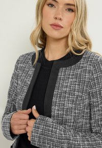 Svart och vit tweedblazer med en texturerad yta, med en fast svart krage och manschetter, designad med en strukturerad passform och långa ärmar.