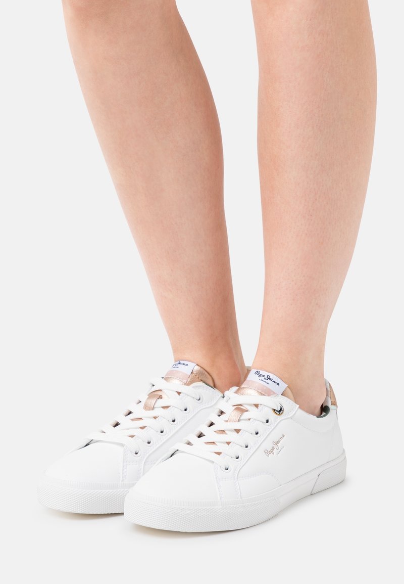 Sneakers bianche con una texture liscia, caratterizzati da dettagli in rosa oro metallizzato e lacci beige. Progettati con una silhouette a basso profilo e una suola in gomma.