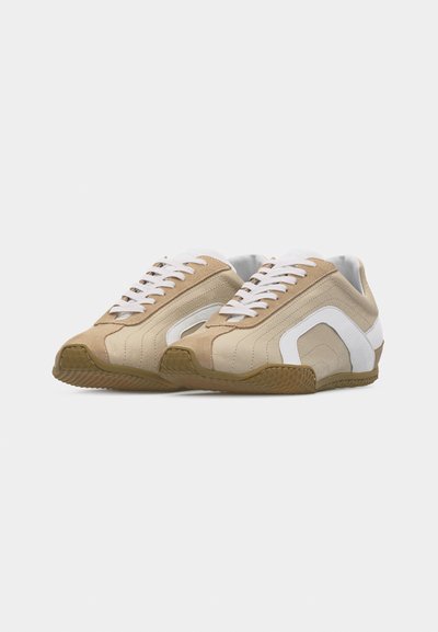 Paire de baskets basses beige et blanche avec des lacets blancs et des semelles en caoutchouc naturel, présentées côte à côte sur un fond blanc.