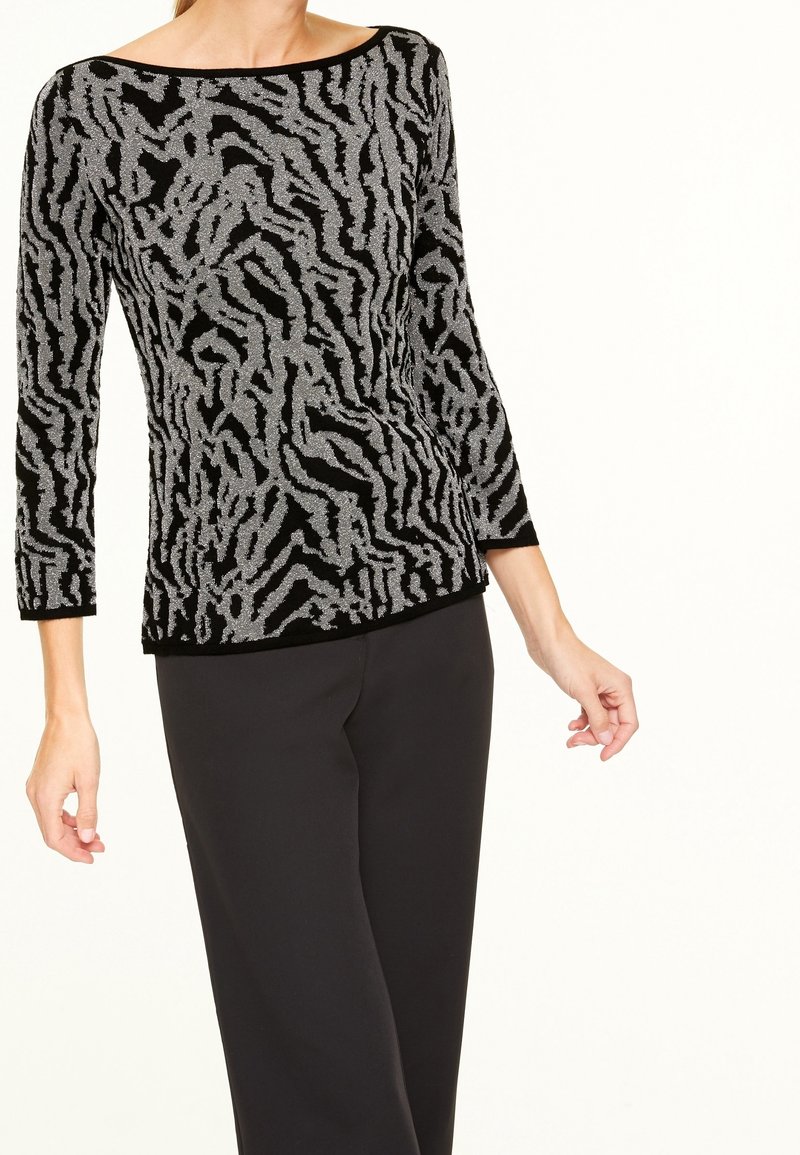 Haut à manches longues noir et argent présentant un motif zèbre texturé, avec un large col bateau et une silhouette ajustée, associé à un pantalon noir.