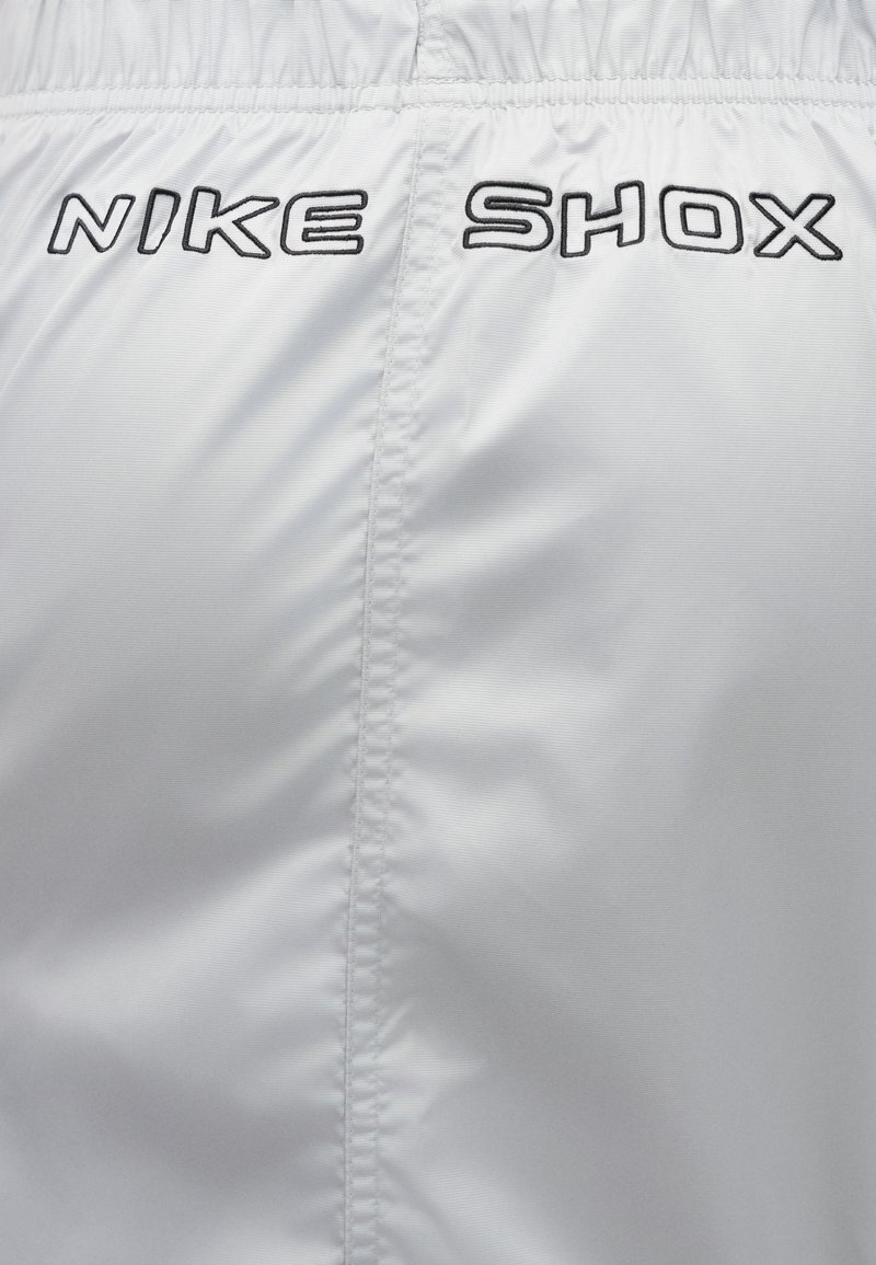Witte Nike Shox shorts met een elastische tailleband, een gladde textuur en een zwart geborduurd "NIKE SHOX"-logo op de achterkant.