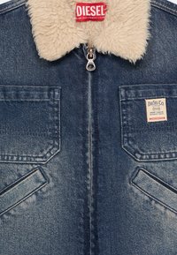 Jaqueta de ganga com colarinho de pelúcia bege, fecho frontal com zip, dois bolsos no peito e etiquetas de logotipo no colarinho e no bolso esquerdo.