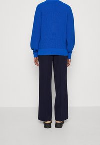 Pull bleu tricoté avec épaules tombantes et ourlet côtelé, associé à un pantalon large bleu marine et des chaussures noires épaisses.