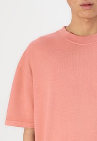 Różowa, oversize'owa koszulka z okrągłym dekoltem i krótkimi rękawami. Wykonana z organicznej bawełny o gładkiej fakturze, z prostymi detalami szycia.