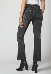 Jeans negros acampanados con cintura alta, que cuentan con bolsillos traseros y un ligero desgastado. Combinados con botines negros de tacón. Textura de denim suave.