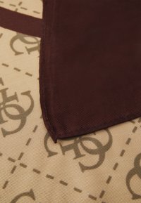 Tissu marron avec un ribbage diagonal, présentant un fond beige avec des motifs de logo plus foncés subtils et des lignes en pointillés. Bords cousus proprement.