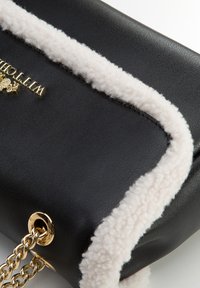 Borsa a mano in finta pelle nera con bordi bianchi pelosi, hardware in tono oro e tracolla a catena. Superficie texturizzata con una forma strutturata.