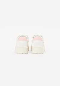 Hvite og rosa sneakers med en glatt overdel, teksturerte detaljer og en tykk, klumpete såle. Bakfra vises tydelige fargeblokker og merking.