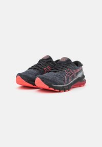 Un par de zapatillas de correr negras y coral con tela de malla, suelas acolchadas y franjas laterales de marca sobre un fondo blanco.
