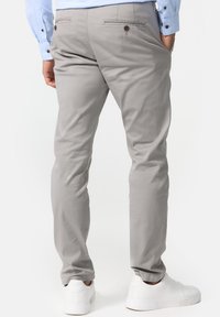 Chino gris clair en tissu tissé lisse, avec une coupe ajustée, des poches arrière avec des boutons, et associés à des baskets blanches.