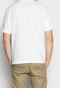 Witte katoenen t-shirt met korte mouwen, ronde halslijn en een eenvoudig ontwerp; details omvatten een kleurrijk logo op de linkermouw.