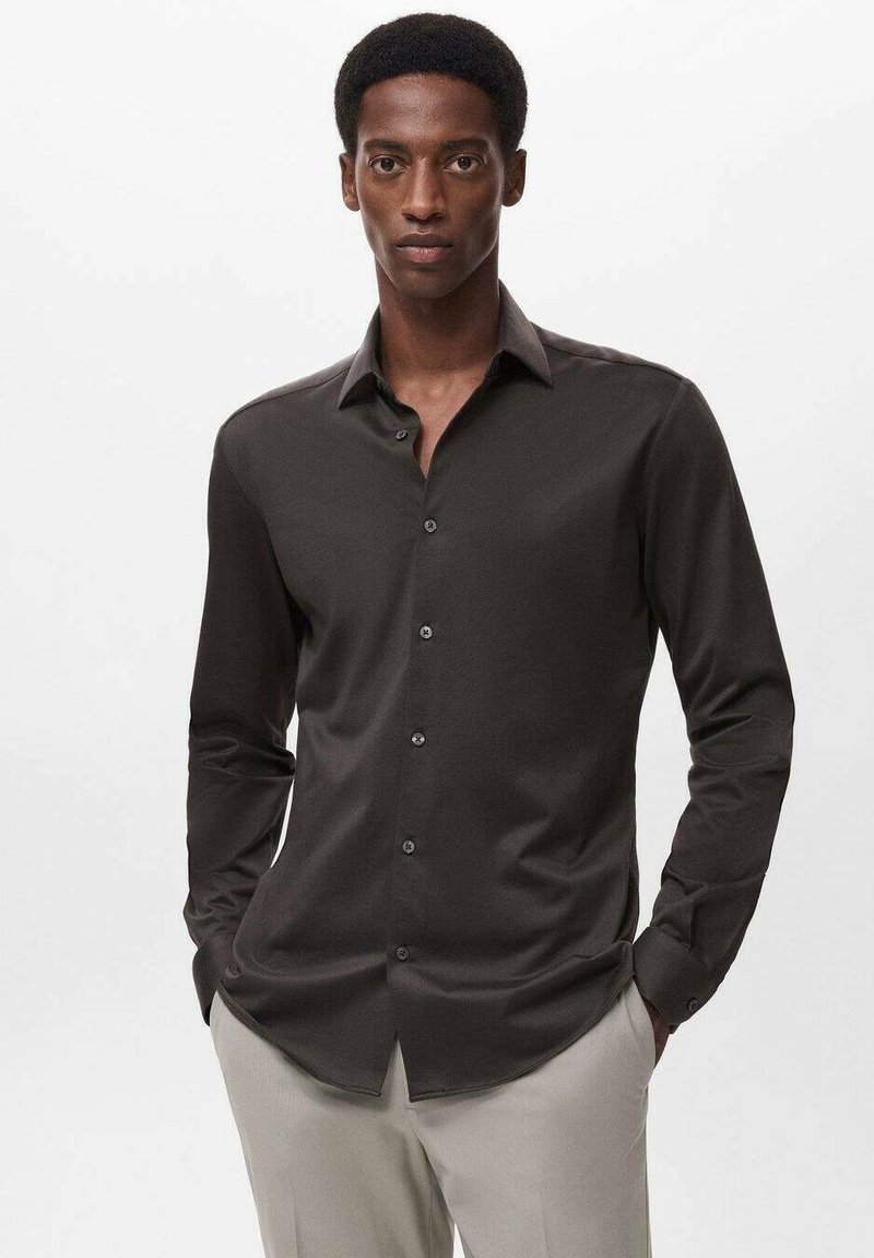 Camisa de manga larga marrón oscuro con cuello abotonado y tapeta frontal, que presenta botones negros y una textura suave.