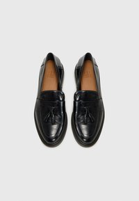 Mocassini in pelle nera con superficie liscia, design flat slip-on e dettagli con nappe sul davanti. Presentano una soletta marrone e bordi cuciti.