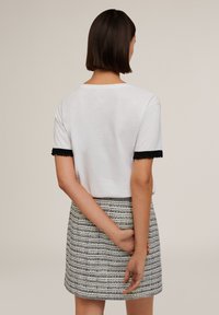 Top blanco de manga corta con acentos de flecos negros en las mangas, combinado con una falda a rayas en colores monocromáticos, con líneas horizontales.