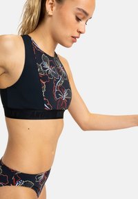 Sujetador deportivo negro con estampado floral, con un cuello alto y una banda ancha con logo. Combinado con braguitas de bikini a juego.