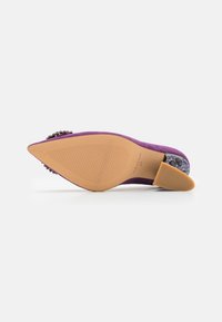 Scarpa con tacco alto in suede viola, punta affusolata, accenti decorativi in gemme e suola in gomma beige con linee testurizzate per una migliore aderenza.