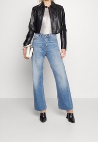 Chaqueta de cuero negra corta, top ajustado plateado, vaqueros de pierna ancha azul claro y zuecos negros con punta. Bolsa blanca con asa.
