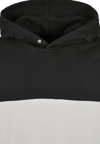 Svart och vit färgblockerad hoodie med en knapp på den svarta huvan, som visar tygtextur och sömdetaljer.