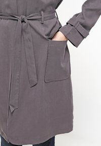 Szary płaszcz z paskiem, o gładkiej fakturze, z długimi rękawami, boczną kieszenią i prostym, uporządkowanym wzornictwem.