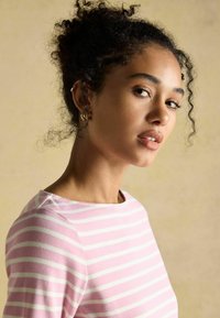 Dlhý rukáv, svetloružový top s bielymi horizontálnymi pruhmi. Mäkka tkanina, okrúhly výstrih, priliehavý strih s jemnou textúrou a zakriveným lemom.