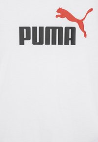 T-shirt en coton blanc avec un grand logo noir "PUMA" et un graphique d'un puma bondissant rouge au-dessus du texte. Design classique à col rond.
