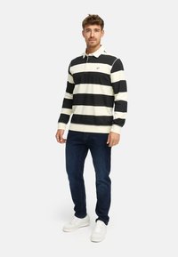 Polo a maniche lunghe a righe bianche e nere con colletto, abbinato a jeans blu scuro e sneakers bianche.
