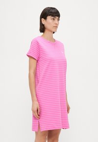 Rausvos dryžuotos suknelės marškiniai su trumpomis rankovėmis, apykakle, šoninėmis skeltuvėmis ir mažu logotipu ant krūtinės. Minkšta, medvilnės struktūra.