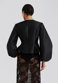 Μαύρο σατέν cropped jacket με όγκους στα μανίκια και εφαρμοστή σχεδίαση στο πίσω μέρος. Συνδυάζεται με διάφανο μαύρο δαντελένιο παντελόνι που δείχνει λουλούδια.