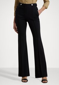Pantaloni neri svasati realizzati in tessuto morbido, con un alta vita e due bottoni bianchi e tasche laterali. Tessuto liscio con design su misura.