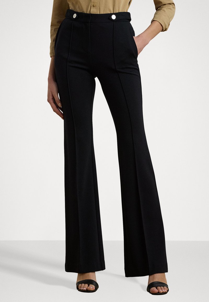 Pantaloni neri svasati realizzati in tessuto morbido, con un alta vita e due bottoni bianchi e tasche laterali. Tessuto liscio con design su misura.