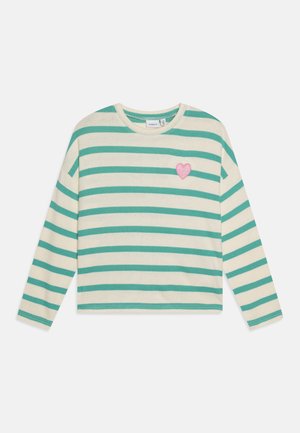 Langermet stripete genser i krem og teal, med et rosa hjerte-lapp på venstre bryst. Laget av myk kvalitet med rund hals.