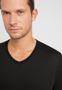 Black v-neck t-shirt made from a smooth fabric, featuring short sleeves and a fitted silhouette. The neckline has a subtle ribbed detail.