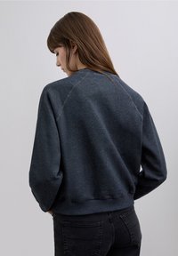 Donkergrijze sweatshirt met een losse pasvorm, voorzien van raglanmouwen, geribbelde boorden en een gladde textuur. Minimale stikseldetails bij de schouders.