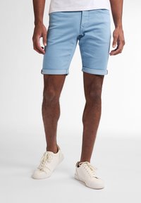 Pantalones cortos de mezclilla azul claro con puños doblados, que cuentan con presillas para cinturón y bolsillos frontales. Combinados con zapatillas off-white.