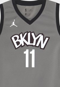Camiseta de baloncesto gris con diseño de cuello en V, que presenta ribetes negros, grandes gráficos en blanco con el número "11" y "BKLYN", y el logo de Jumpman. Material Dri-FIT.