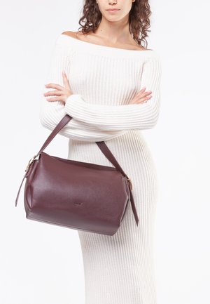 Borsa a tracolla in pelle bordeaux di forma tondeggiante, con manico corto in marrone e una texture sottile. Presenta un design minimalista e un piccolo dettaglio del logo.
