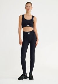 Top corto negro de canalé y leggings de talle alto, que muestran una textura suave, un branding mínimo y un diseño ajustado. Zapatillas deportivas negras.