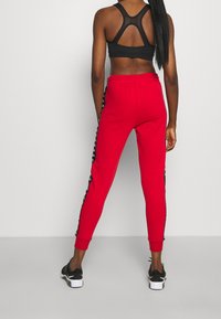 Rode sweatpants met zwarte zijstrepen, getailleerde pasvorm, elastische tailleband, gecombineerd met een zwart sporttop en zwarte sneakers.