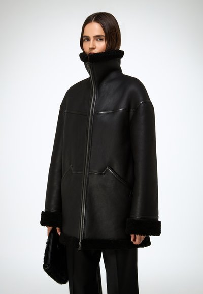 Veste en cuir noir avec un col montant, dotée de poignets en shearling et d'une finition texturée. Comprend une fermeture éclair à l'avant et de grandes poches inclinées.