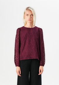 Maroon blouse featuring long, sheer sleeves with leaf-patterned embroidery and a round neckline, paired with black trousers.