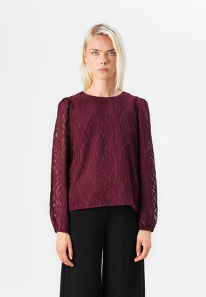 Bordeaux blouse met lange, sheer mouwen met bladerenpatroon borduursel en een ronde halslijn, gecombineerd met zwarte broek.