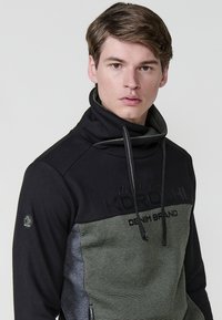 Sudadera de pullover en negro y verde con un alto cuello, tejido texturizado, detalle de logotipo y mangas en contraste. Presenta cordones.