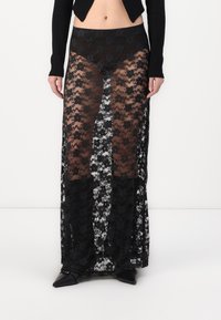 Zwarte maxi rok van kant met een doorschijnend ontwerp, voorzien van bloemmotieven, een zwarte tailleband en stevige zwarte onderbroeken. Te combineren met puntige flats.