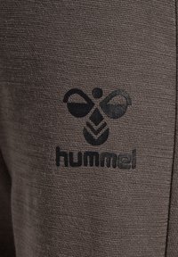 Mörkgråt träningsbyxmaterial med en strukturerad yta; har en svart logotyp av en bi och ordet "hummel" tryckt på.