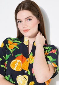 Camisa de manga corta con un fondo azul marino oscuro y un estampado vibrante de frutas, incluyendo naranjas y limones, con un frente abotonado y cuello.