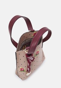 Petit sac à main avec des poignées en cuir bordeaux. Présente un tissu rose pâle avec des pois noirs et des motifs floraux. Fermeture zippée.