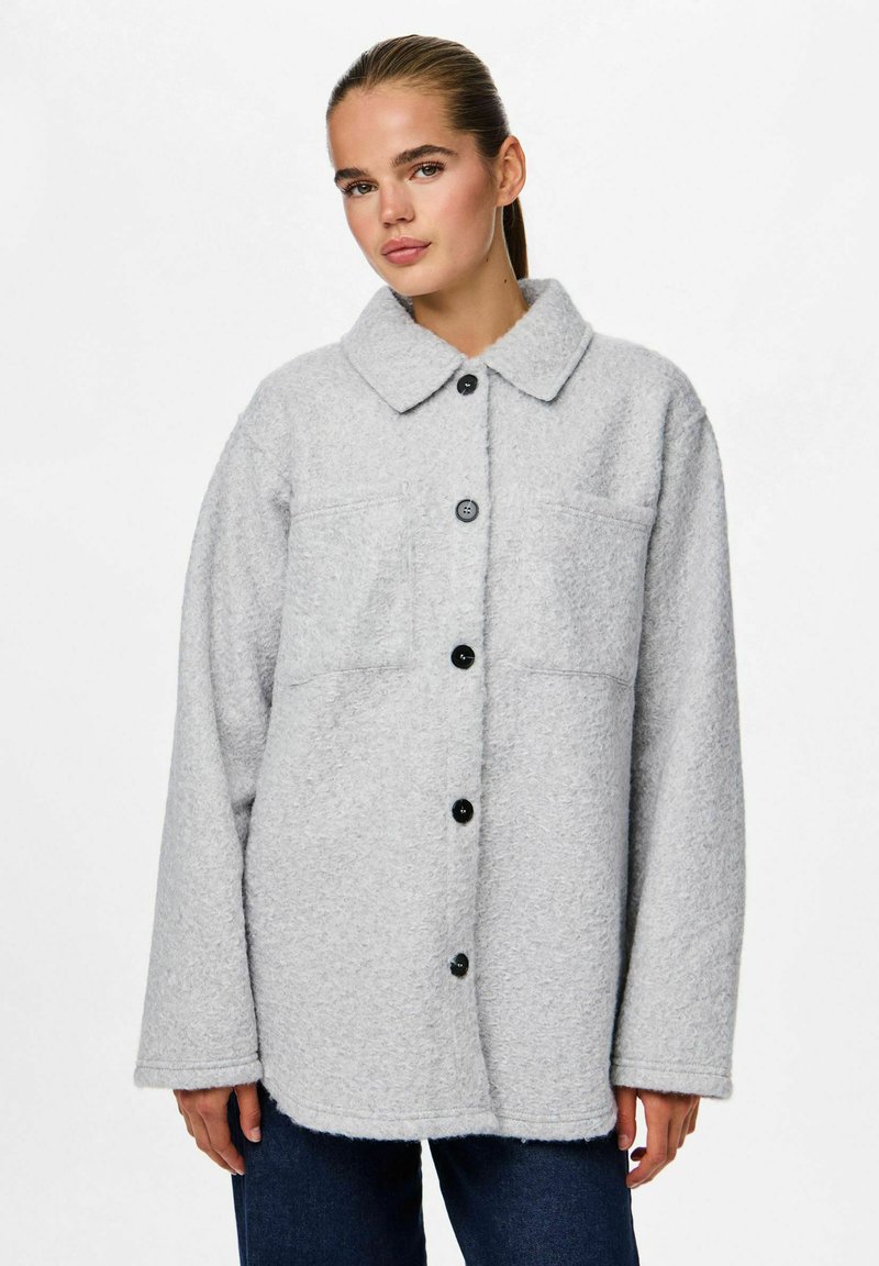 Veste oversize grise claire en tissu texturé, avec un devant à boutons, un grand col et deux poches avant. Boutons noirs inclus.