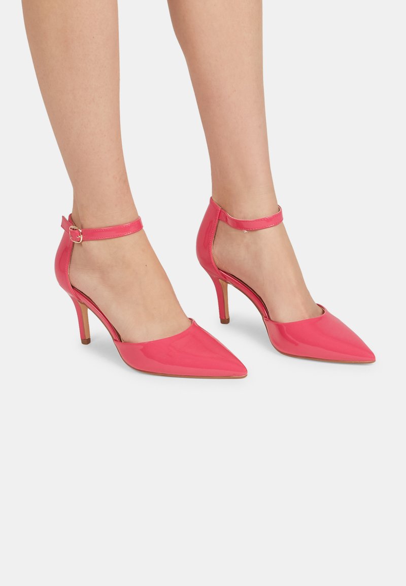 Zapatos de tacón alto de charol rosa con punta afilada, correa al tobillo y un tacón delgado. Textura suave y lados abiertos.