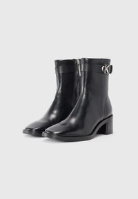 Stivali neri in pelle alla caviglia con punta quadrata, cerniera laterale e cinturino decorativo con dettagli metallici. Tacco spesso per maggiore stabilità.